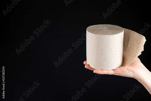 A roll of grey recycled toilet paper on a black background with space for text. The concept of reasonable consumption and use of waste paper.