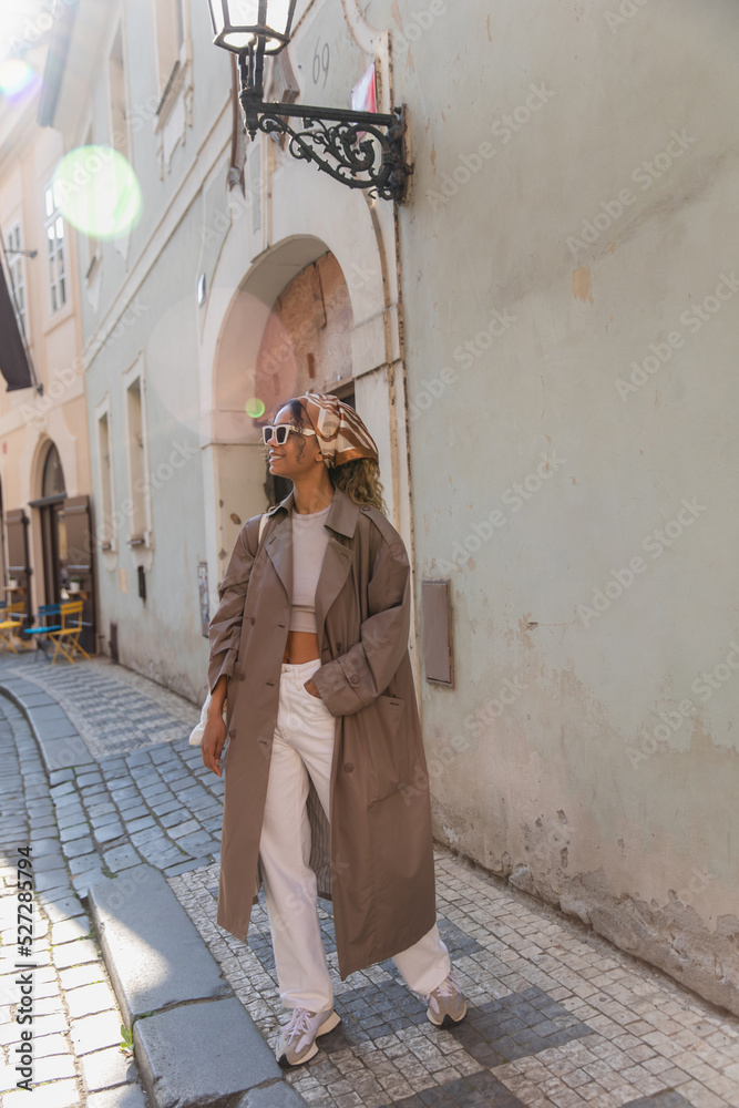 full length of stylish african american woman in trendy accessories posing with hand in pocket on street in prague.