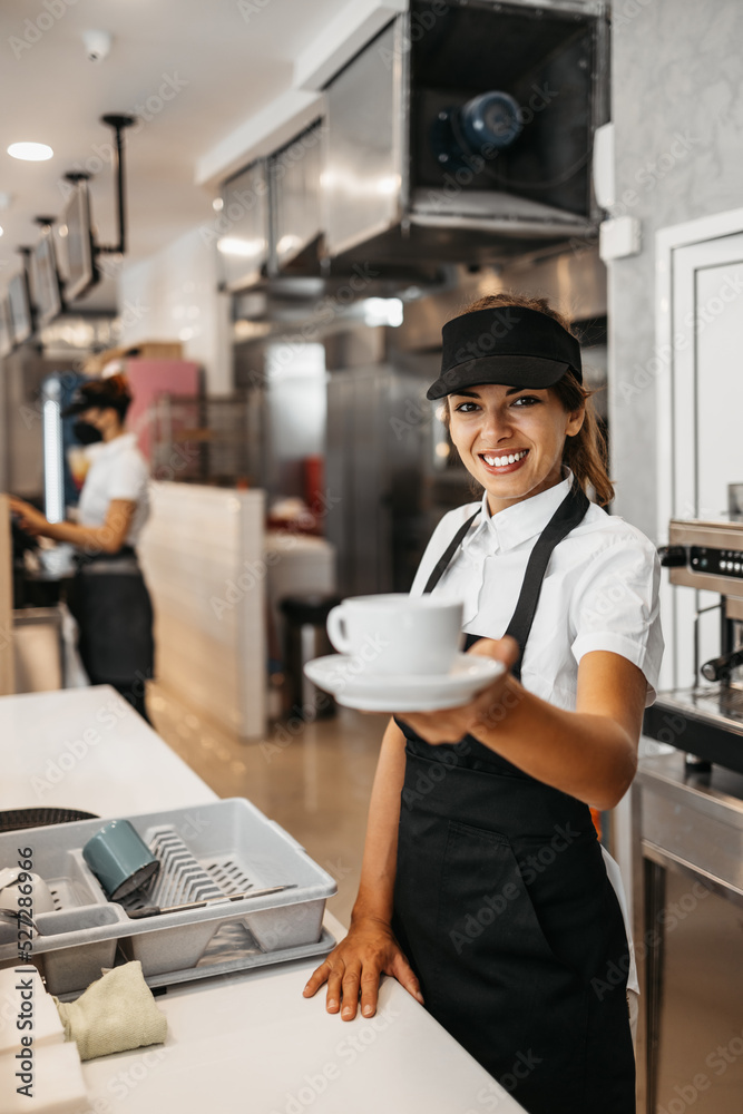 Beautiful and happy young female worker working in a bakery or fast food restaurant and using coffee machine. Positive people in small business concept. Beautiful and happy young female worker working in a bakery or fast food restaurant and using coffee machine. Positive people in small business concept.