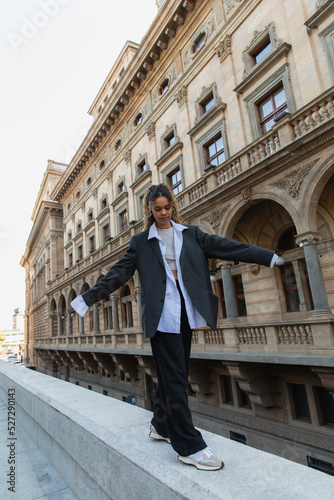 full length of curly african american woman in oversize suit walking with outstretched hands near building of national theater in prague. © LIGHTFIELD STUDIOS