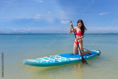 Young woman standing on knees on paddle board for sup surfing in the sea on sunny day,holliday summer vacation concept