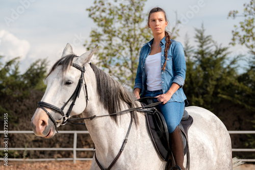 Side view of a woman posing on a white horse in a stable in summer