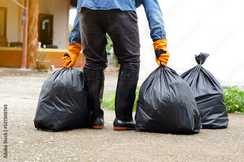 Man throwing out black eco-friendly recyclable trash bag in to big plastic  green garbage container. Stock Photo by nikolast1