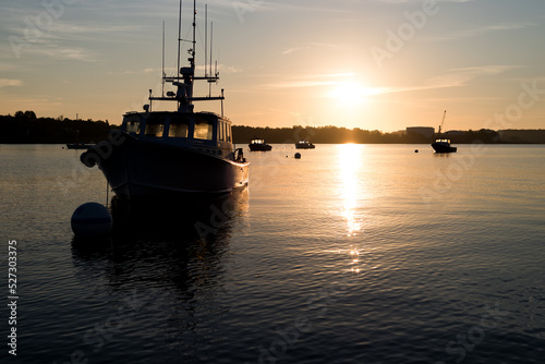 Moored boats at dawn light in Searsport Maine with the sun rising in the background.