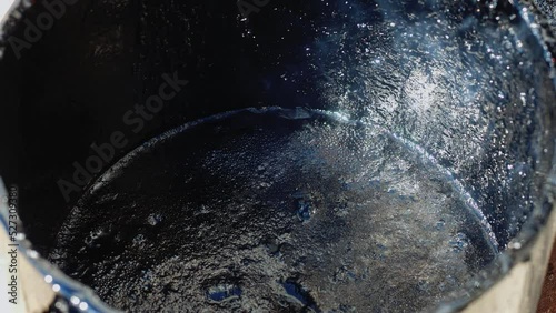 Video 4k. Hot black bitumen or tar boils in round barrel and there is smoke. Close-up. Preparation for repair and pouring cracks on road surface. Road works.