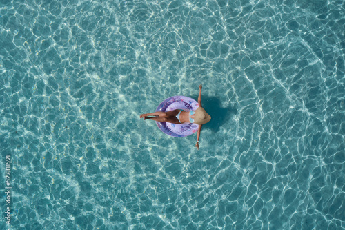 Girl in swimsuit and straw hat  pool ring purple on transparent turquoise water top view. Girl relaxing vacation in the pool top view. Woman on turquoise water aerial view.
