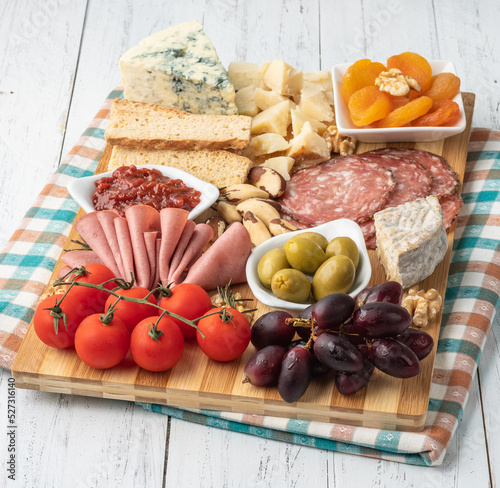 Appetizer board with cheese, nuts, fruits, toasts and charcuterie over wooden table