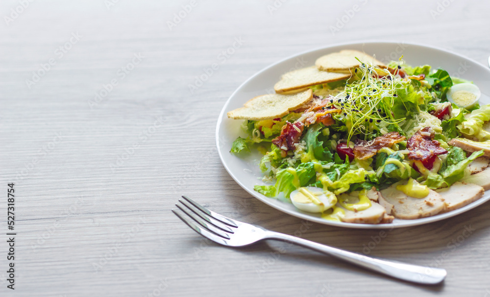 Caesar salad on a white plate. Yellow mustard sauce, quail eggs, herbs, croutons. Front view