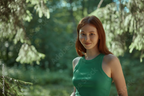 Photo of positive cheerful happy young woman in the woods. Close-up of a red-head girl with freckles. 