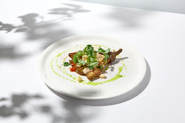 Baked eggplant with cheese on white table with harsh shadows. Aesthetic italian food - baked aubergine on white plate. Stuffed eggplant in minimal style. Stuffed aubergine in vegan menu.