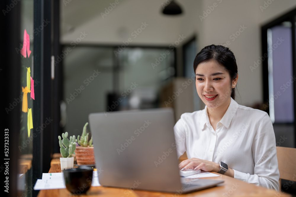 Smile Young business Asian woman freelancer is working her job on a laptop computer in a modern office. Doing accounting analysis report real estate investment data, Financial and tax systems concept. Smile Young business Asian woman freelancer is working her job on a laptop computer in a modern office. Doing accounting analysis report real estate investment data, Financial and tax systems concept.
