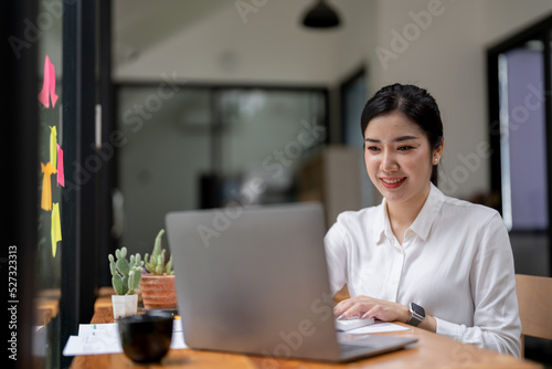 Smile Young business Asian woman freelancer is working her job on a laptop computer in a modern office. Doing accounting analysis report real estate investment data, Financial and tax systems concept.