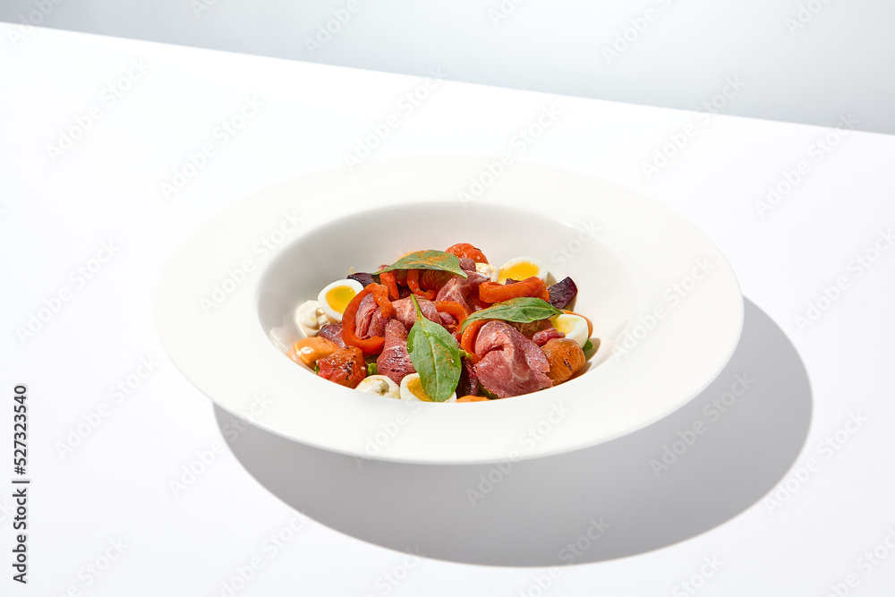Salad with roast beef, vegetables and eggs on white table with harsh shadows. Steak salad in modern style with shadows of leaves. Flashy food. Meat salad with pastrami in summer menu. Salad with roast beef, vegetables and eggs on white table with harsh shadows. Steak salad in modern style with shadows of leaves. Flashy food. Meat salad with pastrami in summer menu.