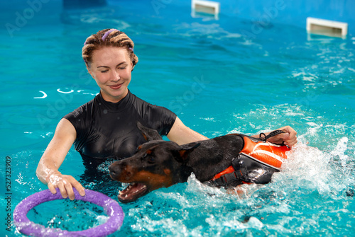 Foto Dog in life jacket swim in the swimming pool with coach