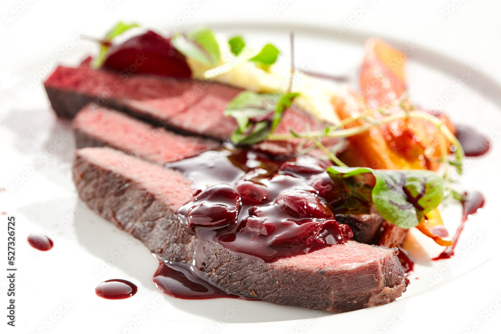 Venison steak with baked vegetables isolated on white plate. Meat steak medium rare roasted with carrot, beetroot and mashed potatoes with cherry sauce. Wild meat in restaurant menu.