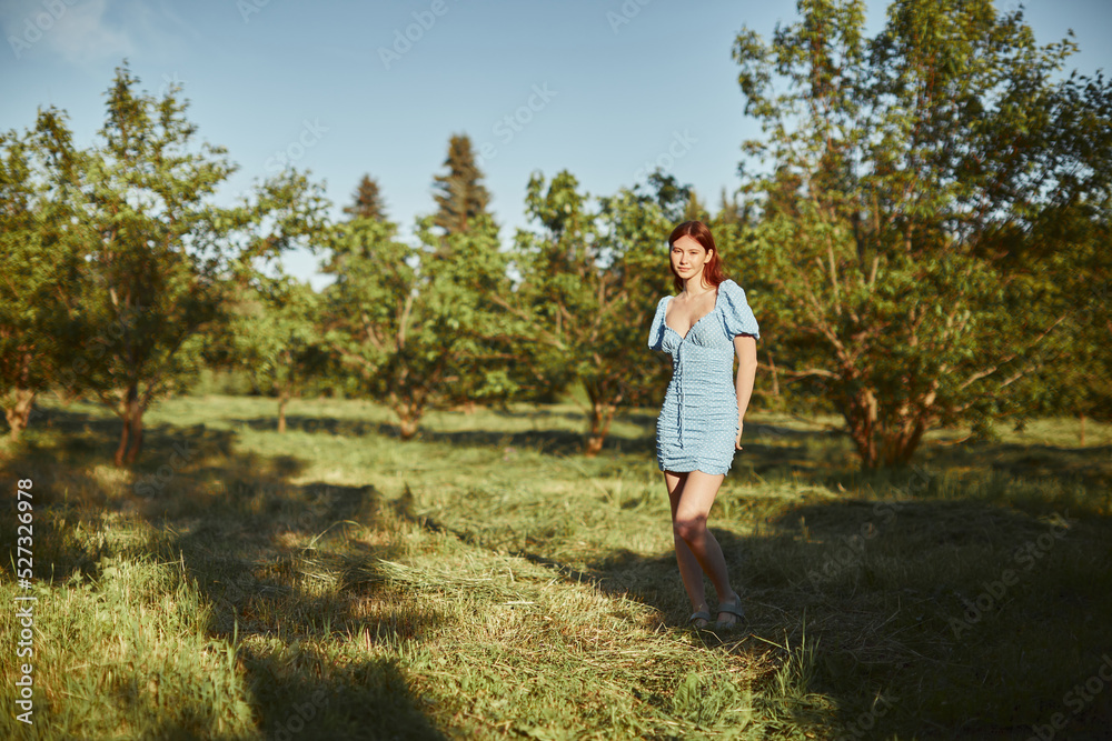 Young beautiful woman walking alone in the forest in blue dress. Enjoying sun and fresh air.