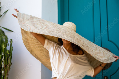 Woman in big straw hat relaxing by entrance door of villa,