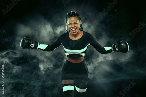Boxing sport concept. Woman with braids on black background with smoke. Girl sportsman muay thai boxer fighting in gloves in gym. Boxing social media post template