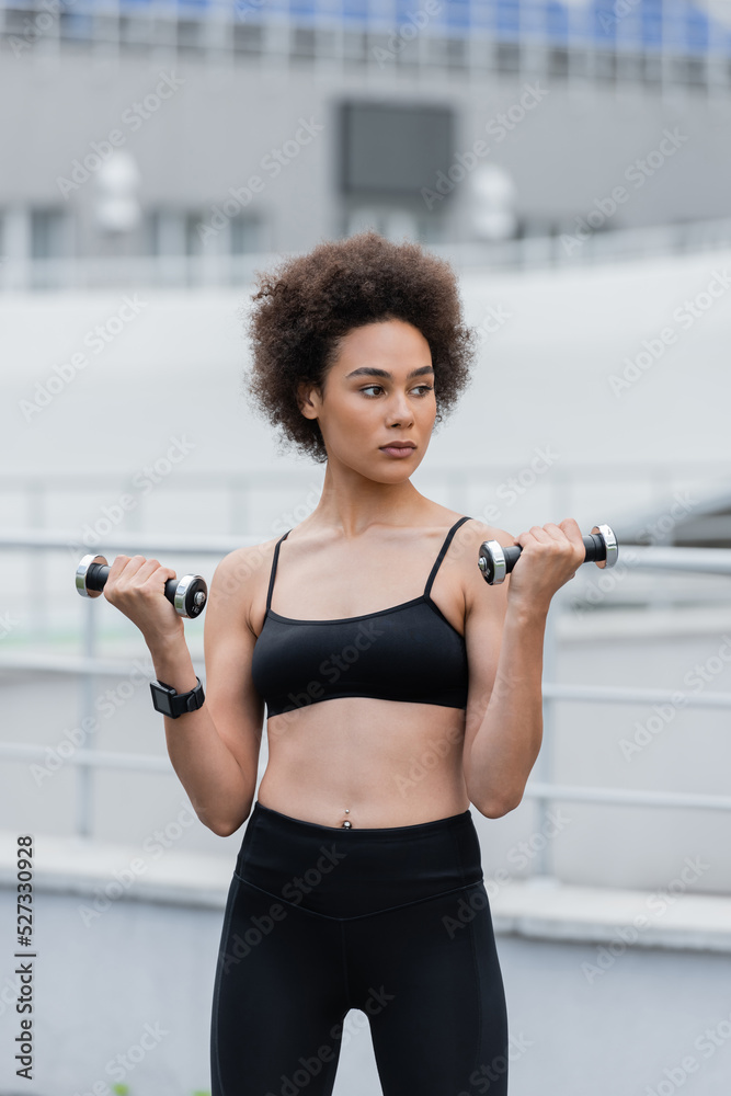athletic african american woman in black sports bra training with dumbbells. athletic african american woman in black sports bra training with dumbbells.