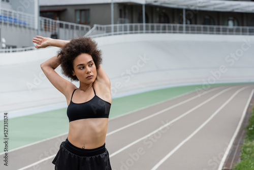 African american sportswoman stretching arms and looking away on stadium.
