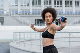 Young african american sportswoman looking at skipping rope on blurred stadium.