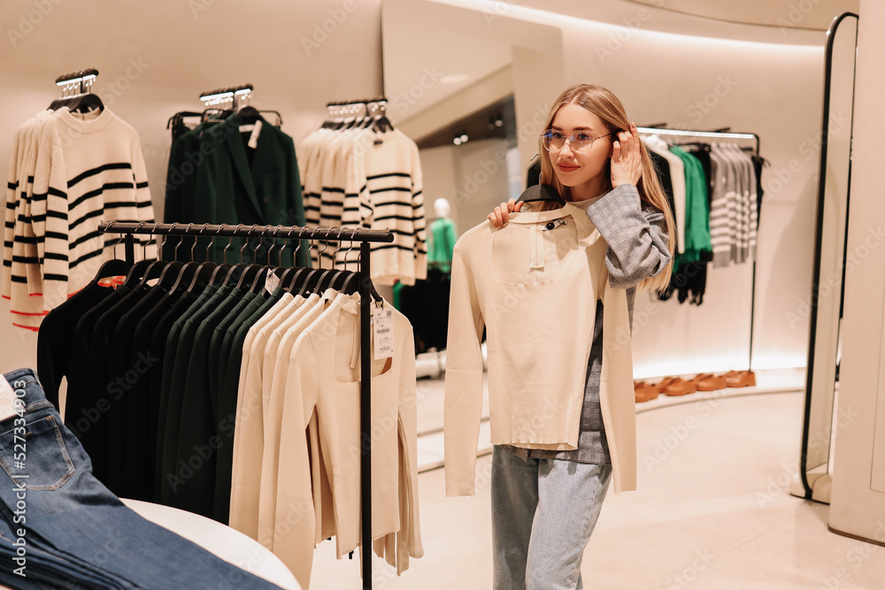 A smiling young shopaholic woman tries on clothes in a shopping mall store, walks through boutiques. Consumerism is a modern problem of society. Anti-environmental