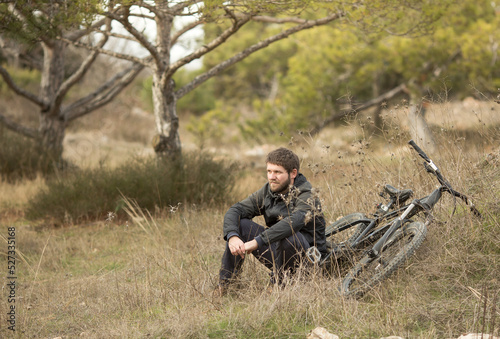 a young man is sitting in a clearing in the forest next to a mountain bike.