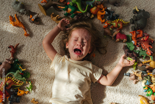 Obraz na plátně Toddler cries and is naughty lying on the floor among toys in the nursery