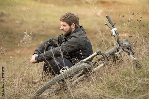 a young man is sitting in a clearing in the forest next to a mountain bike