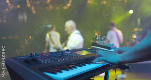 Close up view of musician hand playing synthesizer piano on live concert at stage. The musician playing the electric piano. Music band at background