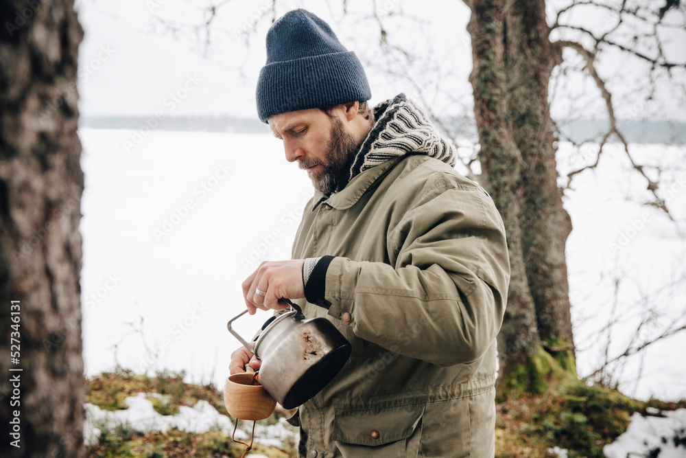 Mature man in warm clothing pouring tea from kettle Mature man in warm clothing pouring tea from kettle