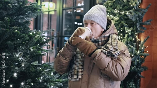 Close-up portrait of an active elderly man drinking coffee on the go, strolling through the decorated city center for the Christmas holidays and New Year.