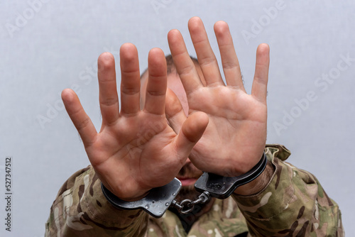 The military man is handcuffed, covers his face with his hands. Concept: war criminal, trial of a serviceman, a crime in the army. photo