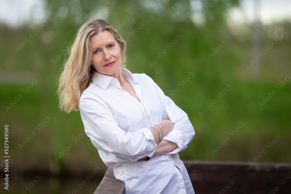 A beautiful middle-aged European woman. Fifty-year-old blonde woman in a white shirt on the background of nature. A beautiful middle-aged European woman. Fifty-year-old blonde woman in a white shirt on the background of nature.