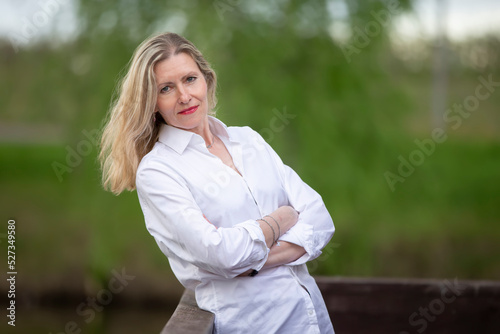 A beautiful middle-aged European woman. Fifty-year-old blonde woman in a white shirt on the background of nature.
