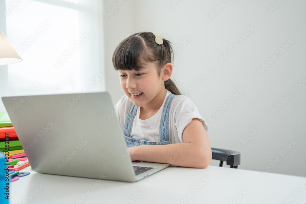 Smiling Asian little girl using laptop doing homework.Child study online on computer at home. Smiling Asian little girl using laptop doing homework.Child study online on computer at home.