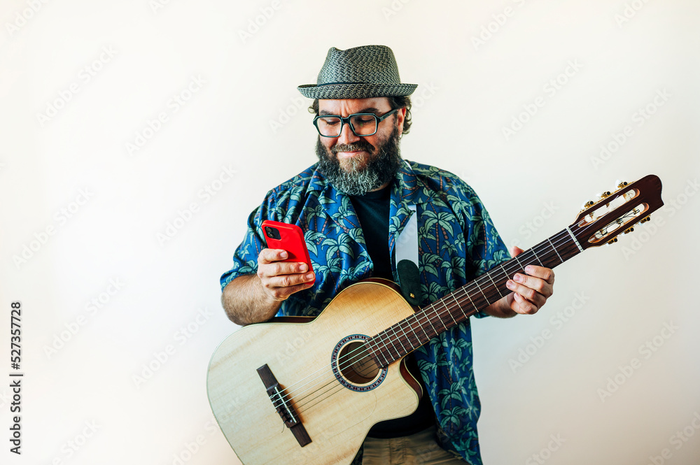Obraz premium Happy bearded man using smartphone with acoustic guitar.