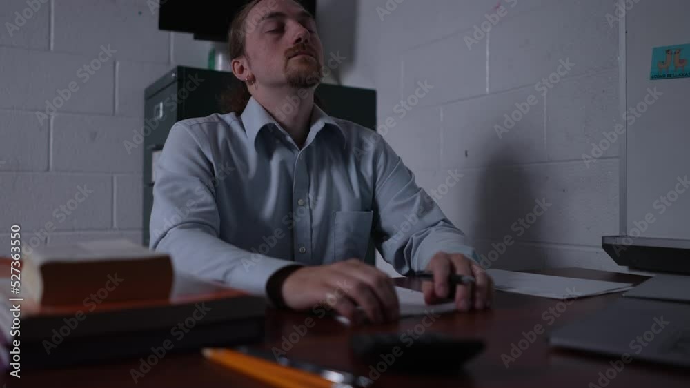 Sad, tired, depressed, fatigued teacher in dark empty classroom grading papers at desk. Sad, tired, depressed, fatigued teacher in dark empty classroom grading papers at desk.