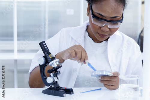 black female doctor student examining and analysis virus test sample on microscope. young biotechnology specialist working in lab. medical science laboratory hospital.