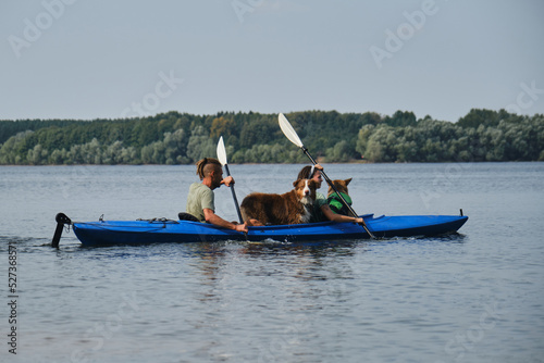 Going kayak boating with dogs on river, active pets concept, happy dog and owner on adventure. Young couple with dreadlocks having fun on vacation with German and Australian Shepherd dogs.