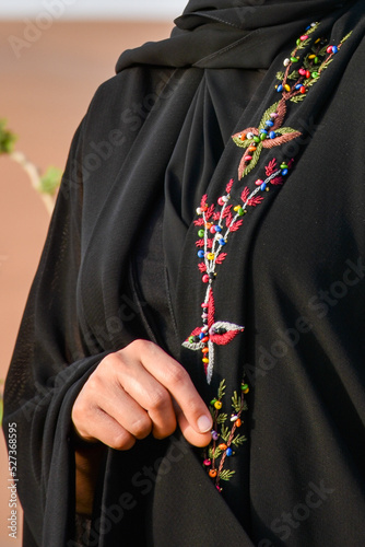 Young woman wearing an abaya and standing in the desert.