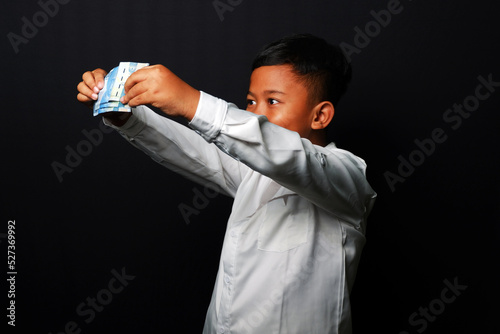 Young kid with confused expression while holding a lot of money isolated on black background. photo