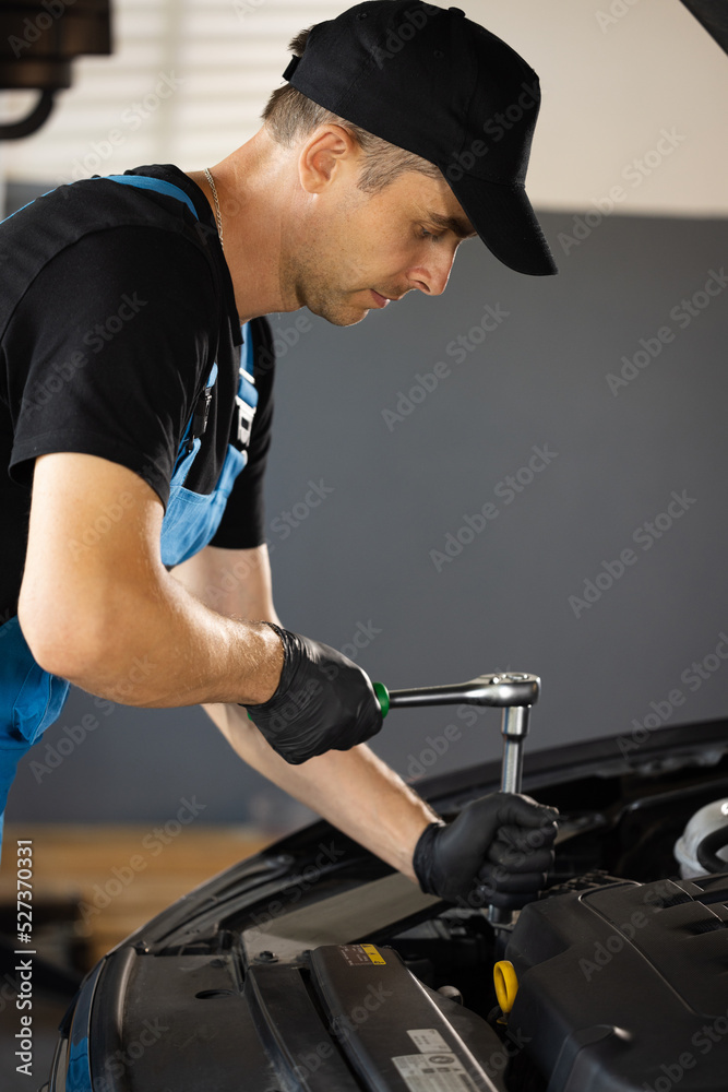 Car mechanic using wrench to repair the engine, car service. Auto service. Empowering male mechanic is working in car service. Man is working on an usual car maintenance. He's using ratchet Car mechanic using wrench to repair the engine, car service. Auto service. Empowering male mechanic is working in car service. Man is working on an usual car maintenance. He's using ratchet