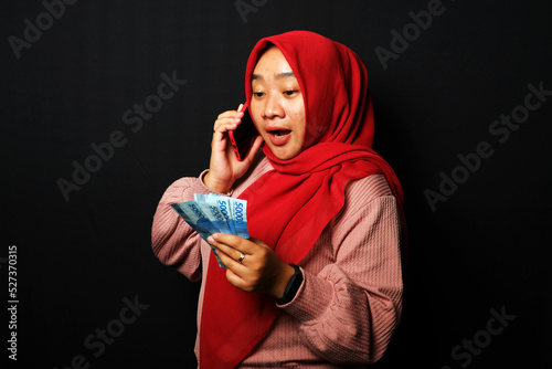 Indonesian woman received a call and holding a lot of money with happy expression isolated on black background. photo