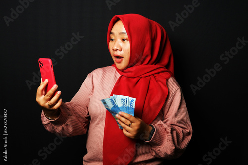 Indonesian woman received a call and holding a lot of money with happy expression isolated on black background. photo