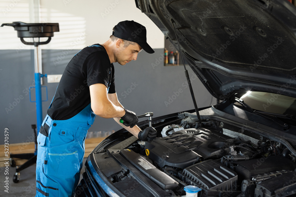 Empowering male mechanic is working in car service. Man is working on an usual car maintenance. He's using ratchet. Car mechanic using wrench to repair the engine, car service. Auto service Empowering male mechanic is working in car service. Man is working on an usual car maintenance. He's using ratchet. Car mechanic using wrench to repair the engine, car service. Auto service