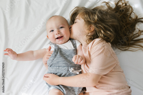 Girl (2-3) kissing and hugging baby brother (6-11 months)