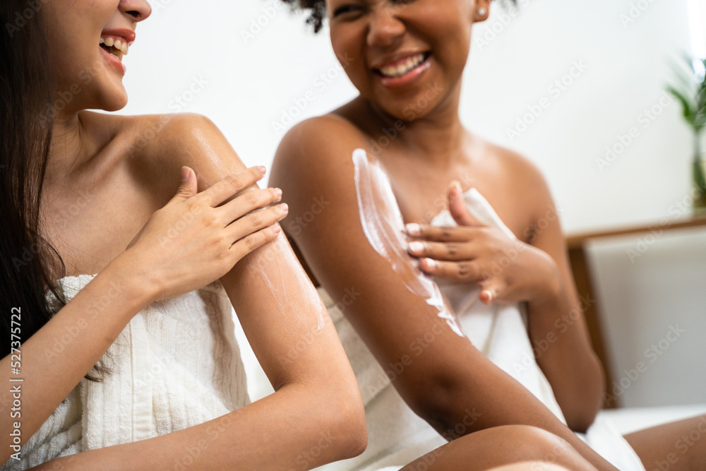 Two multiracial smiling lovely friend women laughing and apply lotion moisturizer cream to each other as diversity friendship and LGBT concept Two multiracial smiling lovely friend women laughing and apply lotion moisturizer cream to each other as diversity friendship and LGBT concept