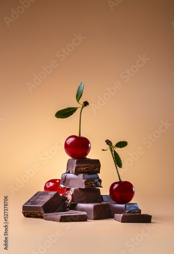 Pieces of dark chocolate and fresh cherry on an orange background. Copy space