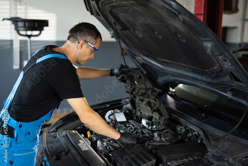 Car mechanic noting repair parts during open car hood engine repair at garage. Mechanic man open a car hood and check up the engine. Overheating of a car engine. Motor with open hood © uflypro